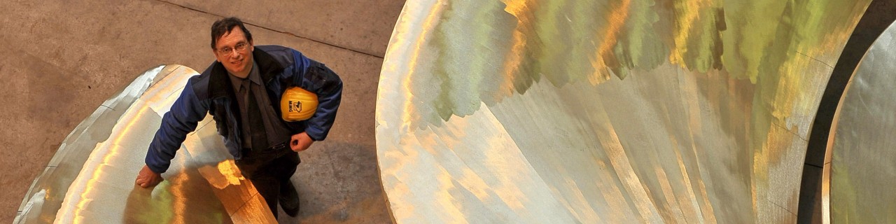 Managing director of a ship propeller manufacturer stands next to a large propeller in a workshop