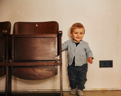 A toddler leaning against an old theater chair