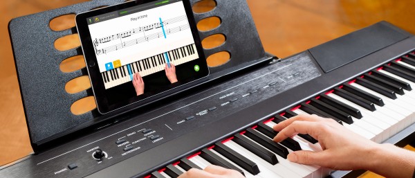 Hände auf E-Piano-Tastatur, auf dem Notenhalter steht ein iPad, auf dem Display sieht man eine Skoove-Lektion