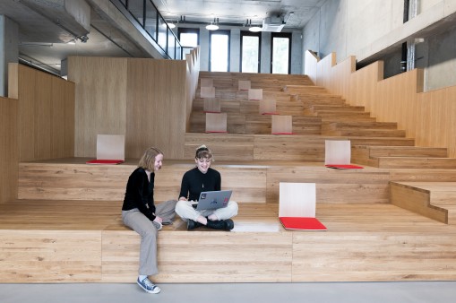 Two women sit on a wooden stand in front of the laptop with a smile