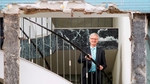 Bürgermeister Armin König ist durch die aufgerissene Wand in einem Haus auf der Treppe stehend zu sehen