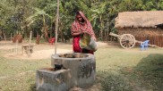 Sheuli Begum gießt einen Eimer Wasser in einen gemauerten Trog, der zu ihrer Biogasanlage gehört