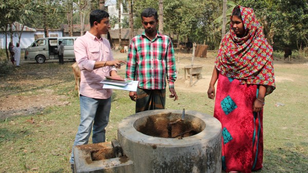 Drei Menschen stehen um den Tank des Biogasherdes und unterhalten sich