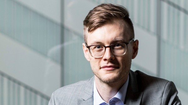 Portrait of Yannik Schreckensberger. The 32-year-old sits on a chair in his office.