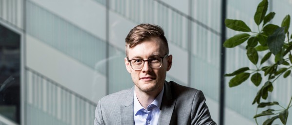 Portrait of Yannik Schreckensberger. The 32-year-old sits on a chair in his office.