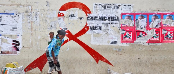 Red Ribbon on a wall, a woman with a child on her back stands in front of it