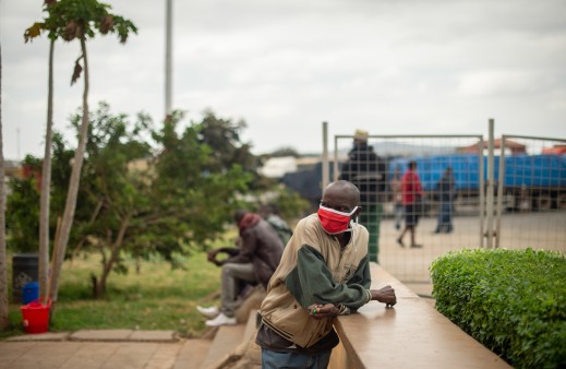 Ein Mann aus Kenia wartet mit einer roten Schutzmaske auf einem öffentlichen Platz