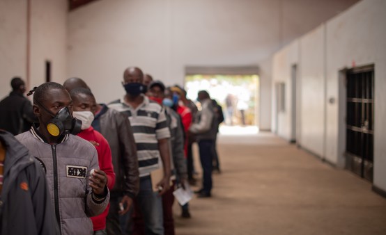 Mehrere Männer mit Mundschutz warten in einer Schlange in Kenia