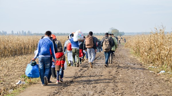 Group of refugees with luggage walking on a dirt road.