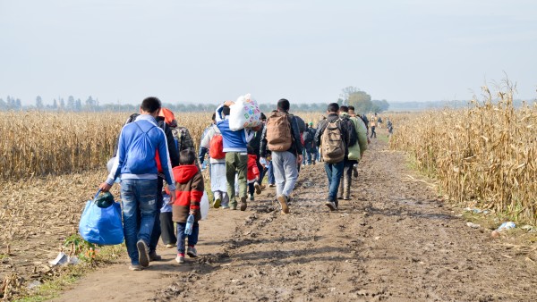 Eine Gruppe Flüchtender läuft mit Gepäck auf einem Feldweg
