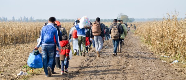 Eine Gruppe Flüchtender läuft mit Gepäck auf einem Feldweg