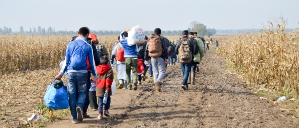 Group of refugees with luggage walking on a dirt road.