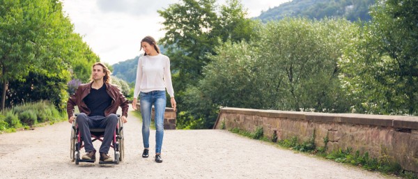 A woman walks alongside a man in a wheelchair