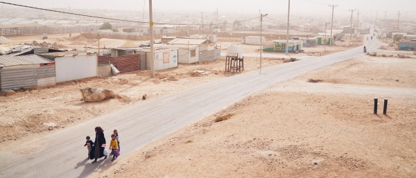 A woman and three children walk down a street in a dust-dry territory