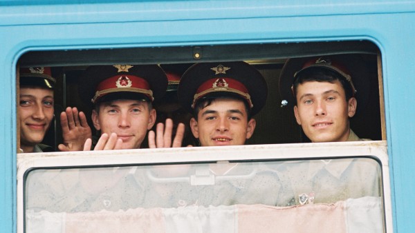 Soviet soldiers smiling and waving from the window of a train. 