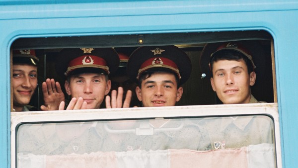 Soviet soldiers smiling and waving from the window of a train. 