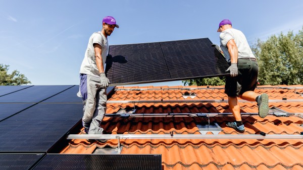 Zwei Installateure heben ein PV-Modul auf ein Hausdach