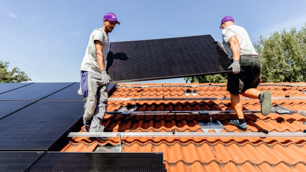 Zwei Installateure heben ein PV-Modul auf ein Hausdach