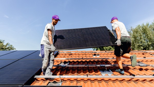 Two installers lift a PV module onto the roof of a house