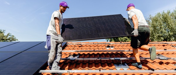 Zwei Installateure heben ein PV-Modul auf ein Hausdach