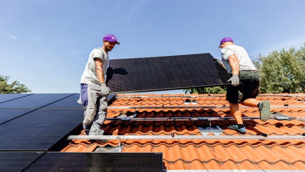 Zwei Installateure heben ein PV-Modul auf ein Hausdach