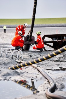 Arbeiter in Arbeitskleidung helfen am Strand vor Büsum das NordLink-Kabel zu verlegen