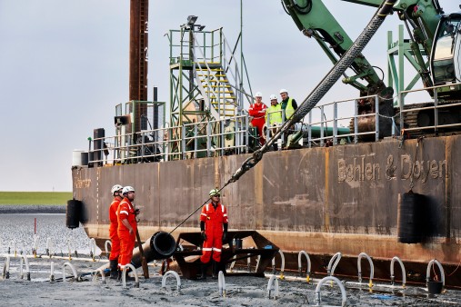 Below the dike in front of Büsum, workers in work clothes lay the NordLink cable in the mudflats.