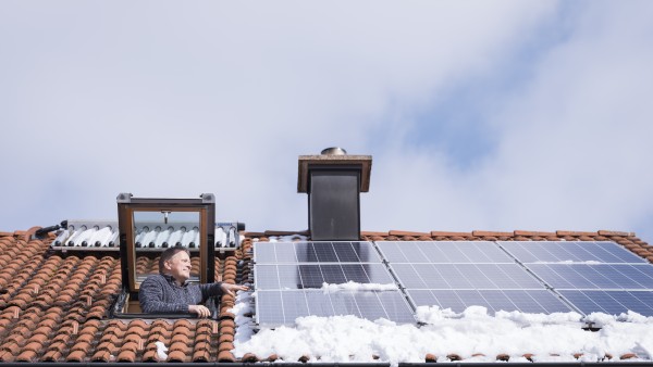A man looks out of his rooftop window onto his photovoltaic modules.