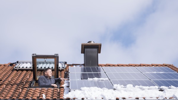 Ein Mann schaut aus einer Dachluke auf seine Photovoltaik-Module.
