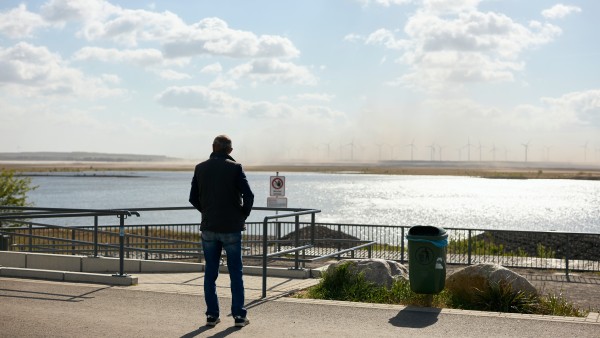 Mann in Rückenansicht, der auf einen See im Hintergrund blickt