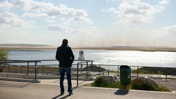 Mann in Rückenansicht, der auf einen See im Hintergrund blickt