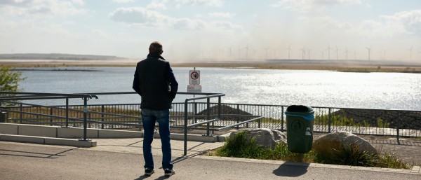 Mann in Rückenansicht, der auf einen See im Hintergrund blickt