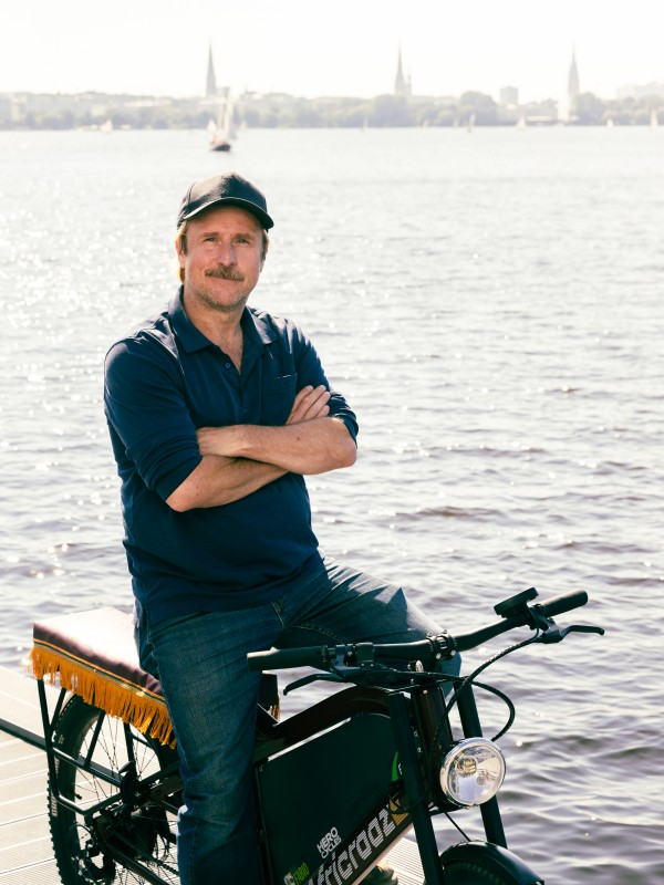 Bjarne Mädel sitzt mit verschränkten Armen auf dem E-Bike und lächelt.