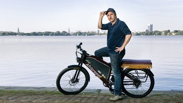 Actor Bjarne Mädel sits on the African E-Bike in front of the Alster