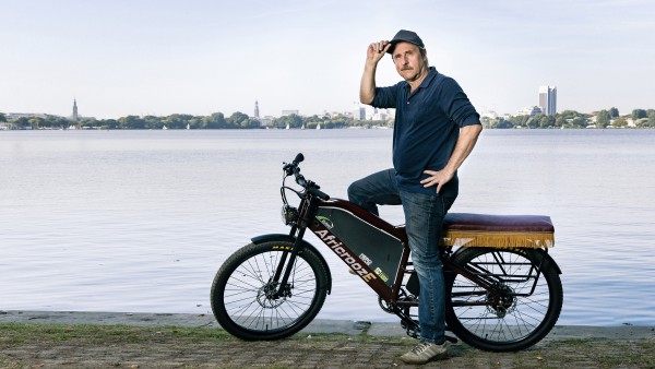 Actor Bjarne Mädel sits on the African E-Bike in front of the Alster