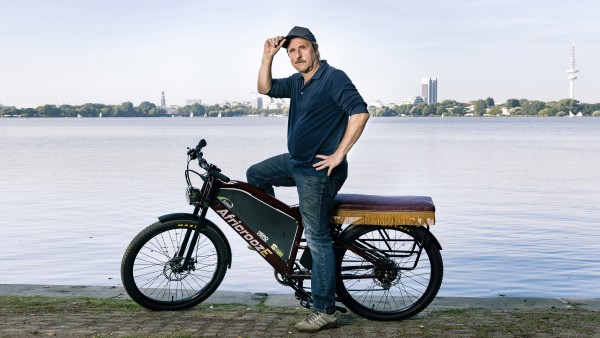 Actor Bjarne Mädel sits on the African E-Bike in front of the Alster