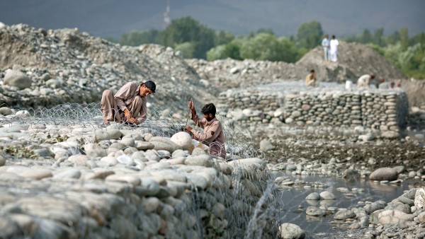Arbeiter befestigen das Ufer eines Flusses mit Steinen und Draht