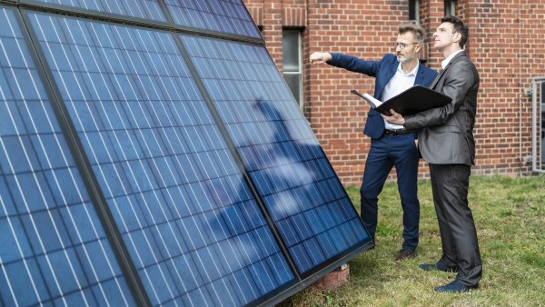 Two businessmen talking outside brick building at solar panels