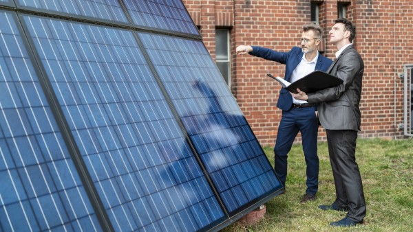 Two businessmen talking outside brick building at solar panels