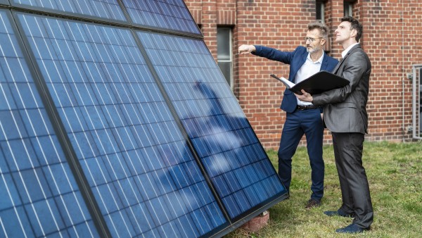 Zwei Geschäftsleute unterhalten sich neben einem Solarpanel vor einem Backsteingebäude