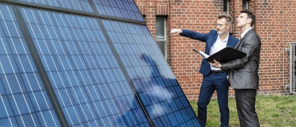 Two businessmen talking outside brick building at solar panels