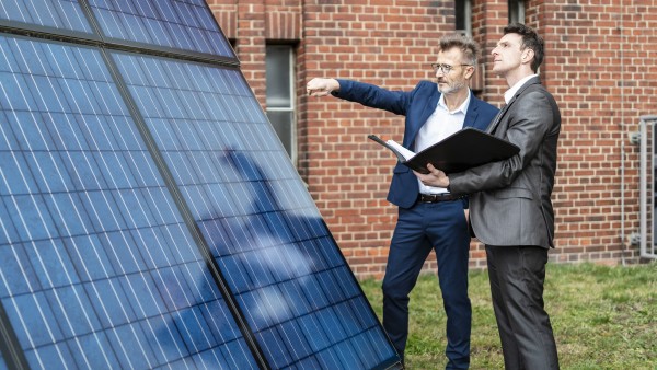 Zwei Geschäftsleute unterhalten sich neben einem Solarpanel vor einem Backsteingebäude