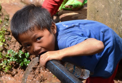 Ein Junge trinkt Wasser direkt aus einem Wasserrohr.