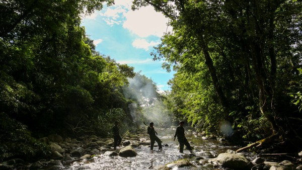 Rangers wade a river in the protected forest of the Annamite Range.