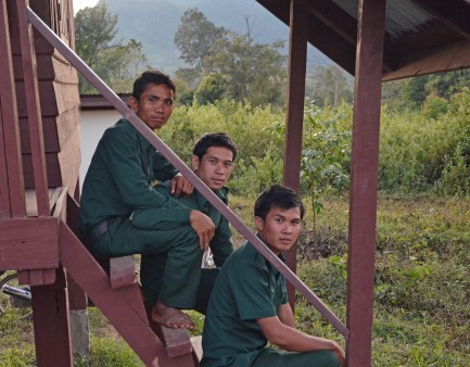 Three rangers sit on stairs in a village in Laos.