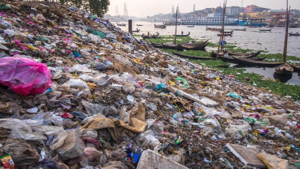 Müll und Plastikverschmutzung am Flussufer in Dhaka, Bangladesch, Flussufer und Boote im Hintergrund