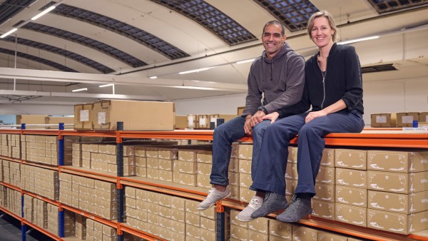 Wildling shoes founders Anna and Ran Yona sit on top of a shelf filled with shoe boxes.