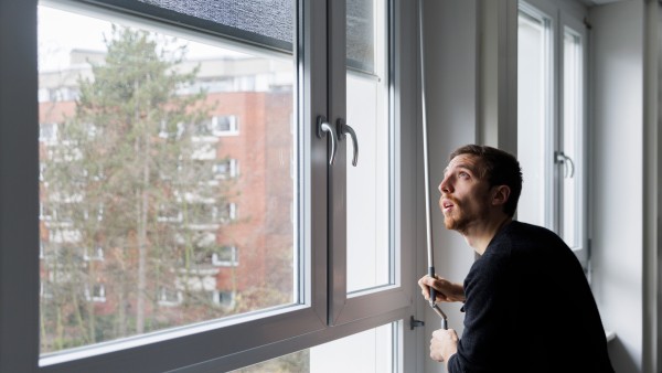 Mann steht am Fenster und kurbelt die Sonnenblende herunter