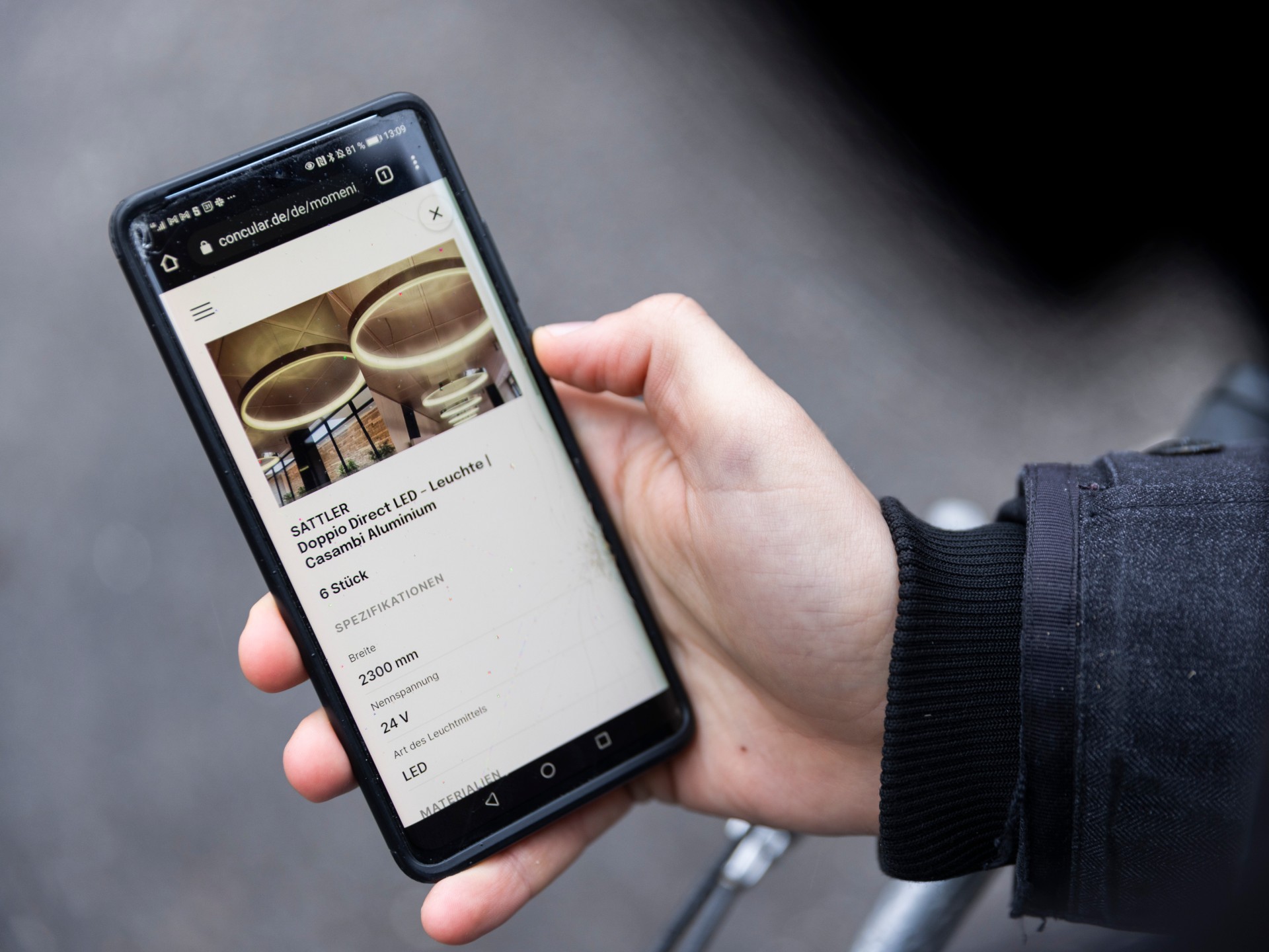 Hand holding a smartphone on which product information on ceiling luminaires is displayed.