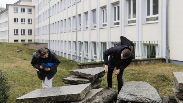 Two people bending over large stone slabs in front of a house